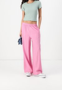 Haut court côtelé vert clair associé à un pantalon ample rose à jambes larges. La tenue comprend une ceinture élastique et des baskets blanches.