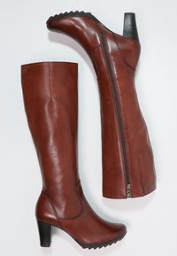 Botas marrones de cuero hasta la rodilla con un diseño elegante, cierre lateral con cremallera, tacón de 4 pulgadas y suela de goma texturizada para mayor agarre.