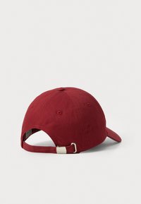 Rode baseballpet van stof. Heeft een afgeronde kroon, contrasterende stiksels en een verstelbare band met een metalen sluiting aan de achterkant.