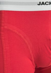 Boxer-bermuda en coton rouge avec une taille élastique blanche portant la marque. Caractéristiques d'une texture lisse et de coutures à plat sur les bords pour plus de confort.