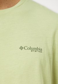 Tricou scurt cu mânecă, de culoare verde deschis, realizat dintr-un material moale, având un logo gri Columbia PFG pe partea stângă a pieptului.