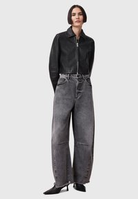 Chaqueta de cuero negra corta, pantalones de mezclilla gris de tiro alto y pierna ancha con dobladillo deshilachado, y tacones negros de punta.