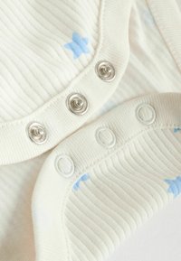 Body crème côtelé avec imprimé d'étoiles bleu clair. Comprend des boutons-pression métalliques et des boutons-pression en plastique blanc au bas pour un habillage facile.