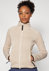 Beige fleecová bunda na zip s vysokým límcem, předními kapsami a černými akcenty; texturovaná tkanina s mírně melírovaným vzhledem.