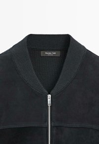 Giacca bomber nera in suede con colletto a coste, zip argentata e design minimalista con dettagli di cucitura strutturata.