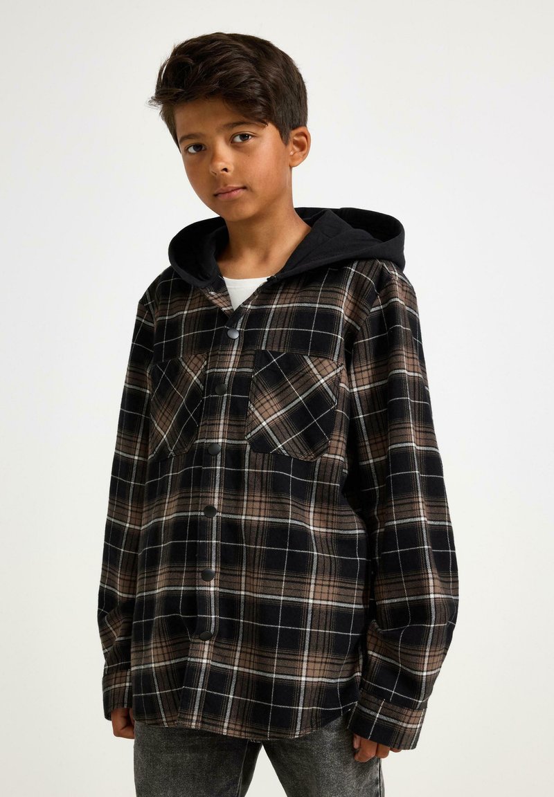 Flannel skjorte i sort og brun ternet, med to brystlommer, en sort hætte og knaplukninger. Blød tekstur og afslappet pasform.