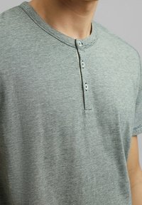 Groene gemêleerde katoenen t-shirt met een ronde halslijn, drie-knopen gesloten placket en korte mouwen. Zachte textuur en subtiele strepen zichtbaar.