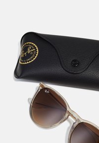 Ray-Ban sunglasses with transparent beige frames and gradient brown lenses, placed beside a black leather case featuring a gold logo.