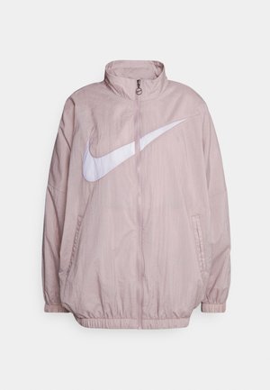 Light pink Nike windbreaker jacket featuring a high collar, full zip closure, and a large white logo on the front. Elastic cuffs and hem.