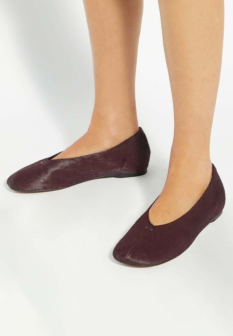 Burgundy flats made of textured fabric with a low-cut design and a rounded toe. The shoes feature a flexible sole and minimal detailing.