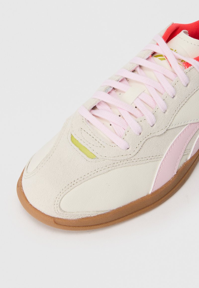 Sneaker con tomaia in pelle bianca e suede beige, lacci rosa e un accento giallo. Presenta una suola in gomma marrone e linee di design eleganti.