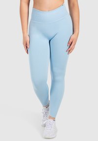 Jasnoniebieskie legginsy z wysokim stanem, wykonane z elastycznego materiału, charakteryzujące się gładką strukturą i dopasowanym krojem, zestawione z białymi butami sportowymi.