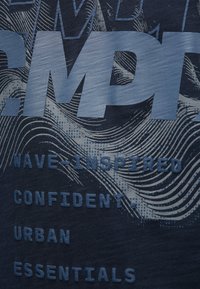 Marineblaue Textilie mit großen, geprägten hellblauen Buchstaben und Wellenmustern sowie texturierten Akzenten, die Phrasen wie "WELLEN-INSPIERIERT" hervorheben.