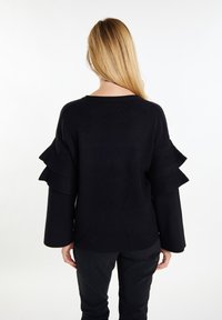 Czarny sweter z wieloma falbaniastymi akcentami na rękawach, luźny krój i teksturowana dzianina. Prosty i elegancki design.