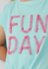 Helles blaues T-Shirt mit pinken, flauschigen Textbuchstaben, die "FUN DAY" buchstabieren. Kurzärmelig und mit rundem Halsausschnitt.