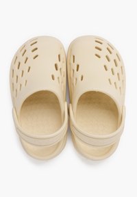 Zoccoli color beige chiaro realizzati in materiale flessibile, con fori di ventilazione sulla parte superiore, texture a motivi all'interno e una fascia posteriore per una vestibilità sicura.