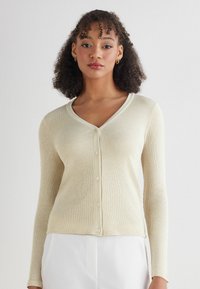 Kremowy kardigan z prążkowanej tkaniny, z długimi rękawami, dekoltem w kształcie litery V i sześcioma guzikami z przodu. Miękka tekstura i dopasowany krój.