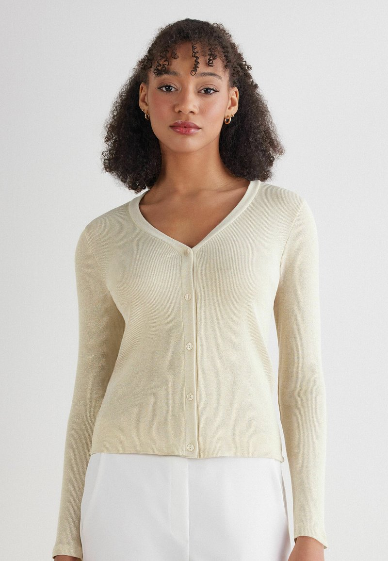 Kremowy kardigan z prążkowanej tkaniny, z długimi rękawami, dekoltem w kształcie litery V i sześcioma guzikami z przodu. Miękka tekstura i dopasowany krój.