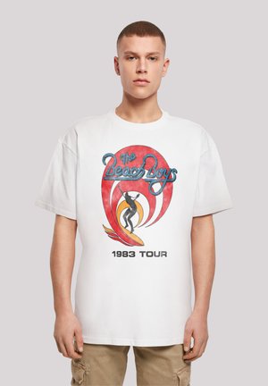 White cotton t-shirt featuring multicolored graphic design with "The Beach Boys" and a surfer, labeled "1983 Tour" in bold black text.