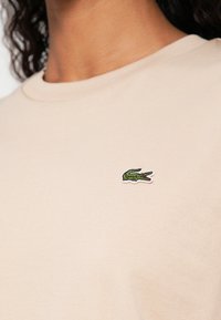 T-shirt de algodão bege claro com um pequeno logótipo bordado de crocodilo verde e branco no peito esquerdo. Design com decote redondo.