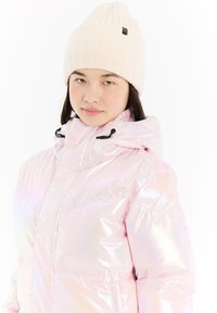 Iridescent pink pufferjakke med høj krave og justerbar hætte, parret med en ribbet cremet strikhue med et sort mærke.