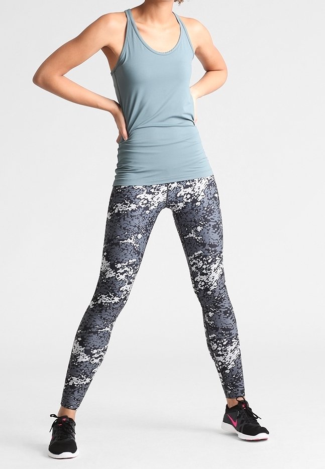 Vaaleansininen hihaton paita, jossa on istuva muotoilu, yhdistettynä mustiin ja harmaisiin camokuvioisiin leggins-leggingseihin, ja viimeistelty mustilla urheilukengillä.