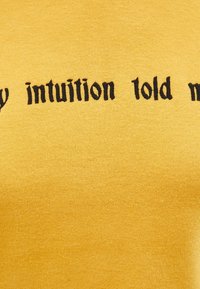 Tela amarilla con texto bordado en negro que dice "la intuición me dijo" en un estilo de fuente gótica.
