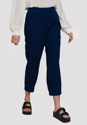 Námořnické modré zkrácené kalhoty s elastickým pasem, šňůrkou, předními kapsami a uvolněným střihem, stylizované s bílou blůzou a černými sandály.