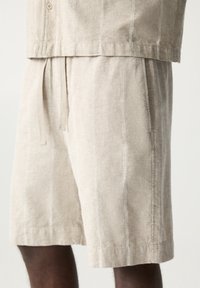 Beige linnen shorts met een losse pasvorm, voorzien van verticale gestructureerde strepen, zijzakken en een tailleriem voor verstelbare maat.