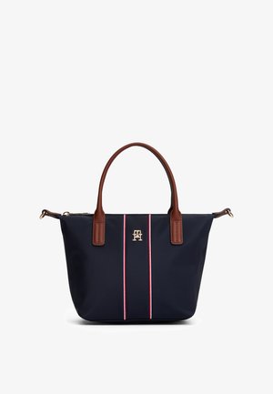 Navy blue tote bag with two brown handles, red, white, and blue vertical stripes, and a small gold logo centered on the front.