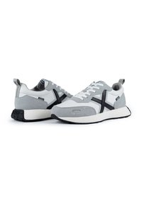 Zapatillas gris y blancas con materiales de ante y textil, que presentan una franja negra de acento, punta redonda y cordones blancos sobre una suela de goma.
