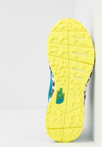 Semelle extérieure jaune vif avec motifs de grip texturés ; dessus bleu et noir avec des accents blancs et un logo, affichant un design robuste pour l'extérieur.