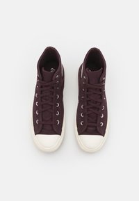 Sapatilhas altas em tecido bordeaux escuro com solas de borracha brancas, apresentando ilhós metálicos e atacadores combinando. Design simples e clássico.