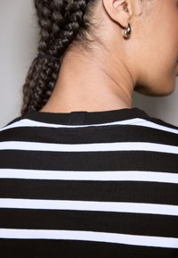 Mustvalgete triipudega topp ümarate kaelustega, tagaküljel nähtava riputuskonksuga. Sile tekstuur, keskmise raskusega kangas.