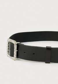 Musta nahkavyö, jossa on neliömäinen hopeinen solki, joka on koristeltu kirkkailla strasseilla ja sileällä pintakuvioinnilla, sekä säätöreiät koon mukaan.