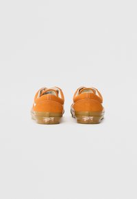 Orange suede sneakers with a rubber sole, featuring a rounded shape, stitched accents, and logo on the heel, viewed from the back.