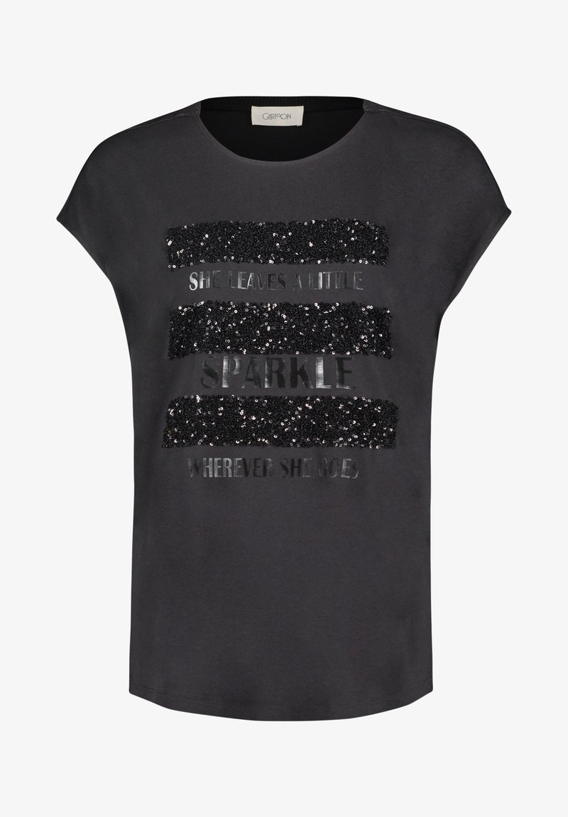 T-shirt gris à manches courtes, avec un design en sequins et en texte métallique qui indique "ELLE LAISSE UN PETIT ÉCLAT PARTOUT OÙ ELLE VA."