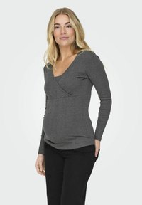 Grauer Langarmtop mit V-Ausschnitt und Wickeldesign, aus weichem Stoff, geeignet für Umstandsmode. Schwarze Hose ergänzt das Outfit.