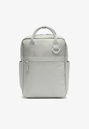 Mochila cuadrada gris claro con asas superiores, bolsillo frontal con cremallera, bolsillos laterales y un anillo de metal en la correa frontal.