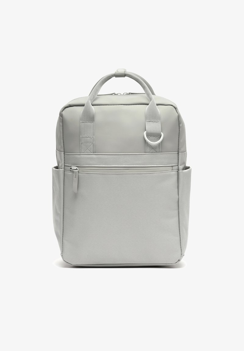 Světle šedý čtvercový batoh s horními madly, předním kapsou na zip, bočními kapsami a kovovým kroužkem na předním popruhu.