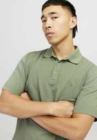 Polo shirt verde khaki con pettorale bottonato, maniche corte e un sottile logo sul petto. Tessuto di cotone liscio.