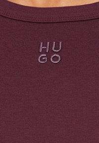 Μπορντό ριμπ πλεκτό πουκάμισο με το κέντημα "HUGO" σε νήμα που ταιριάζει στον λαιμό. Ομαλή υφή, εφαρμοστό σχέδιο.