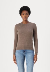 Maglione marrone a maniche lunghe in tessuto morbido con scollatura rotonda, polsini e orlo a costine. Abbinato a jeans blu chiaro.