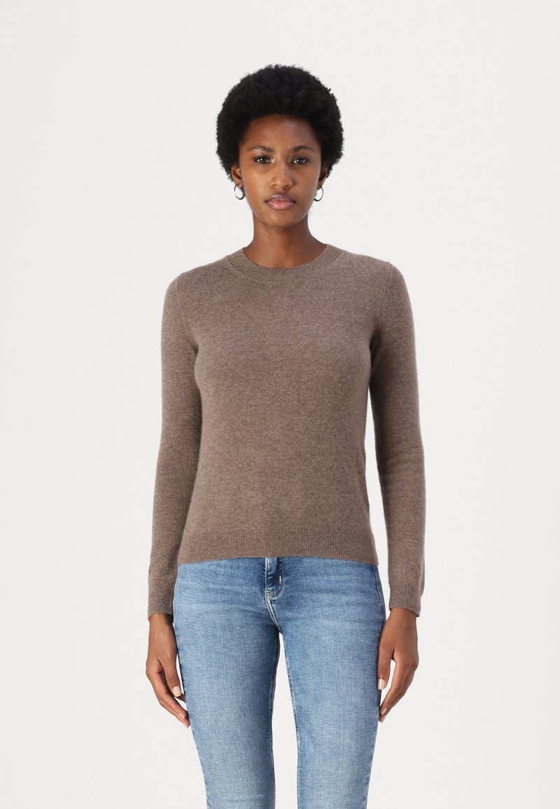 Maglione marrone a maniche lunghe in tessuto morbido con scollatura rotonda, polsini e orlo a costine. Abbinato a jeans blu chiaro.