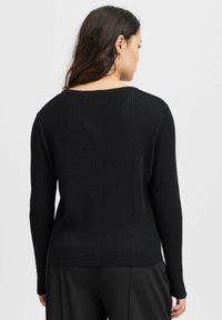 Svart ribbad tröja med rund halsringning och långa ärmar, med en texturerad tyg. Bakdelen har en avslappnad passform och subtila sömdetaljer.