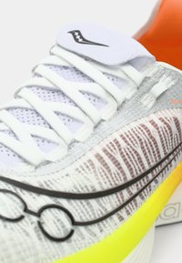 Baskets légères de sport en gris avec un dessus en tricot texturé, des lacets blancs et une semelle multicolore avec des accents jaunes et orange.