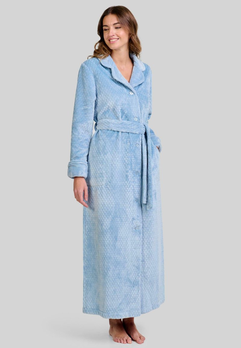 Túnica larga de color azul claro en tela difusa con un patrón texturizado, cuello de chal, botones en la parte delantera, cinturón de lazo y bolsillos laterales. Apariencia suave y cálida.