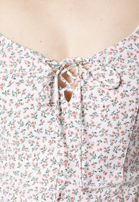 Blomsterkjole i let stof med hvid baggrund, prydet med små lyserøde blomster og grønne blade. V-hals med snoredetalje.