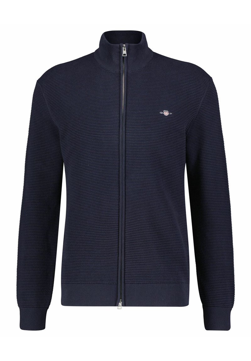 Marineblaue, gerippte Zip-Jacke mit hohem Kragen und Logodetail auf der linken Brust. Sie hat lange Ärmel und besteht aus einem strukturierten Strickmaterial.