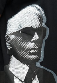 Ασπρόμαυρο πορτρέτο με τεχνοτροπία ημιτόνου ενός άνδρα που φορά γυαλιά ηλίου, τυπωμένο σε σκουρόχρωμο υφασμάτινο φόντο.